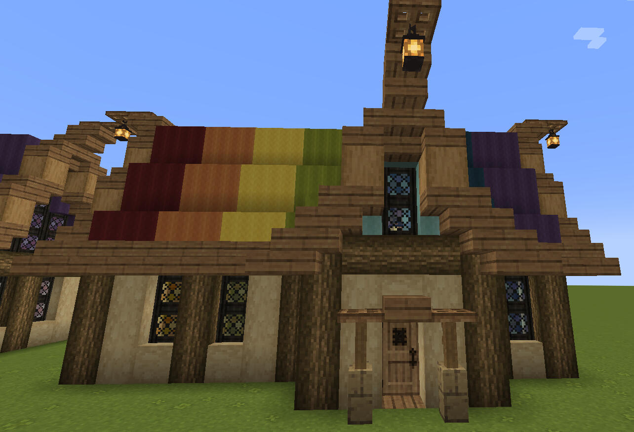 An image of the wood and wool shop, jokingly referred to as the WaW shop. The roof is multicolored wool stripes, with a cozy rustic feel. there are 4 stained glass windows, each stained to match the wool color above it. The build is primarily in striped bi