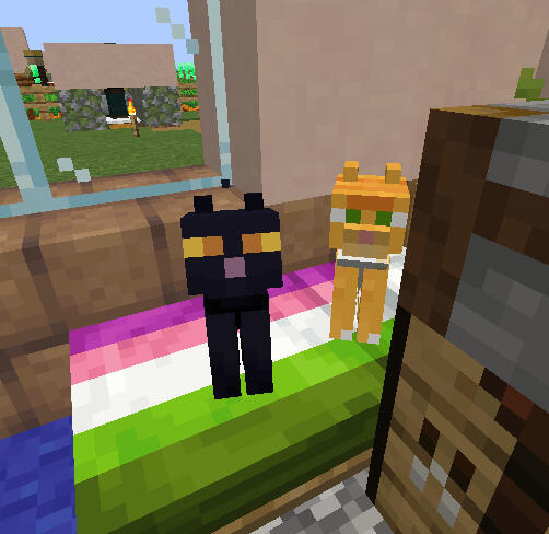 A picture of two cats on a multicolored bed, looking at the camera. The cat closer to the screen is a black cat with orange eyes, and the other cat, seeming to hide behind a crafting table and stone cutter, is orange with green eyes. outside the window is